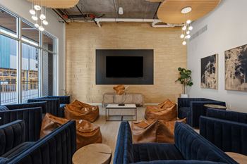 A room with a flat screen tv mounted on a brick wall and a row of blue velvet chairs.